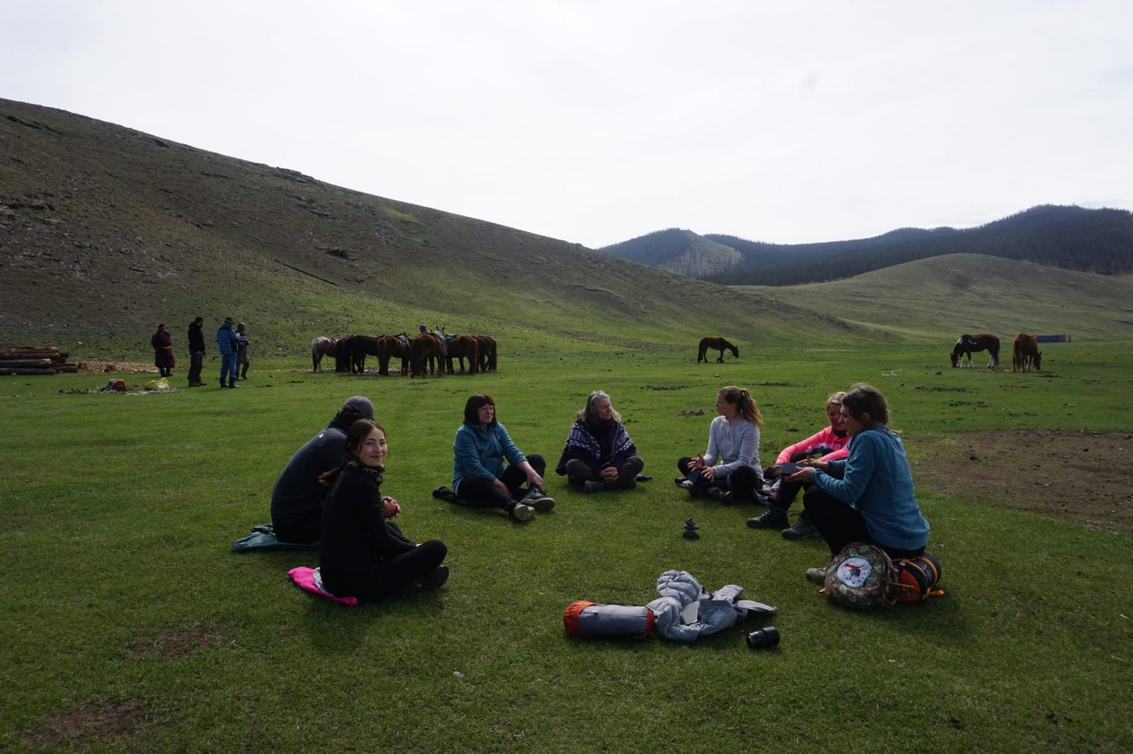 Groupe assis en cercle dans la steppe, chevaux en arrière-plan